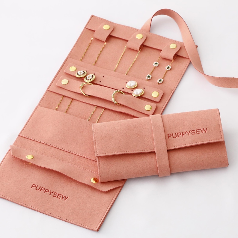 May include: A pink jewelry organizer with multiple compartments and a matching pouch. The organizer is open, displaying various gold necklaces, earrings, and rings. The word "PUPPYSEW" is printed on the pouch and the organizer.
